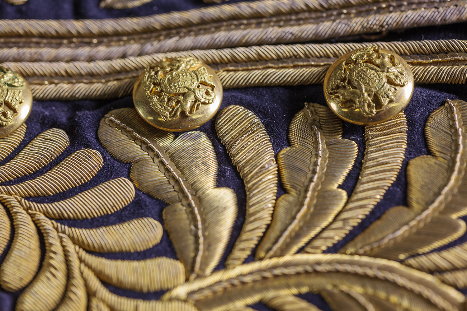 A close-up of an ornate coat with gold embroidered leaves and gold buttons embossed with the Australian coat of arms.