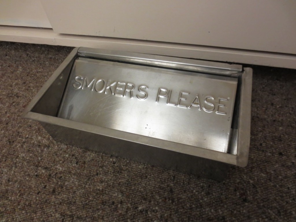 A metal floor ashtray with the inscription 'SMOKERS PLEASE'.