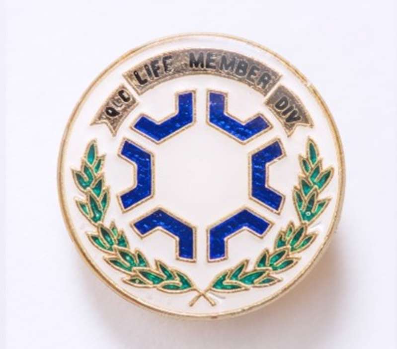 A round pin with a laurel wreath, a pattern of blue shapes, and the words 'Life Member, QLD Div'.