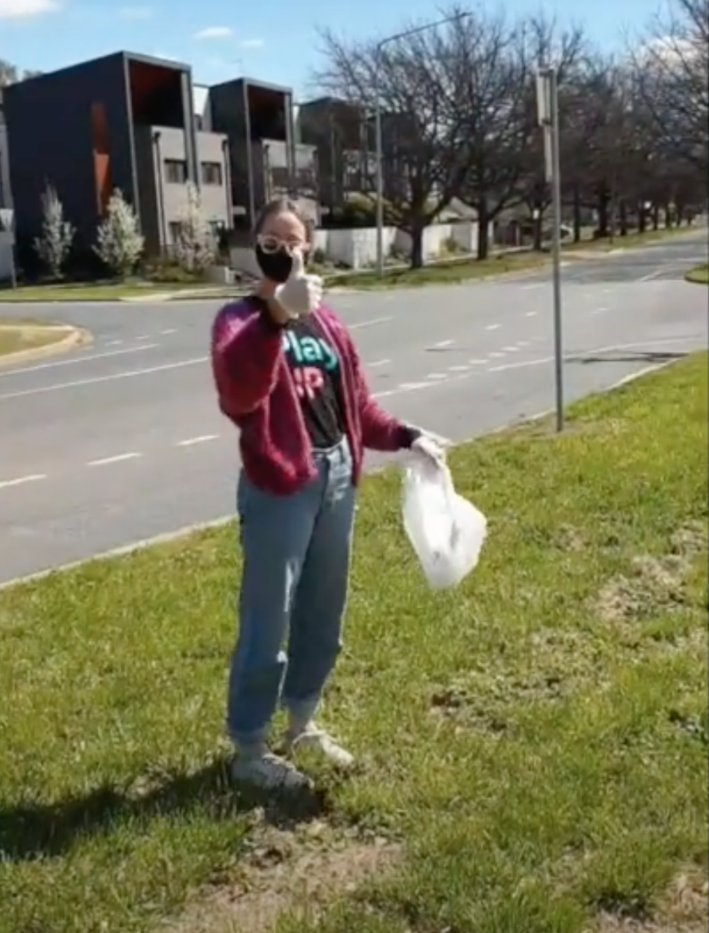 A woman starts outside with a black shirt that says 'PlayUP' and is holding a plastic rubbish bag.