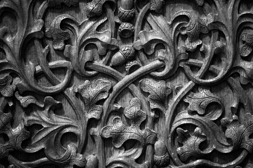 Black and white close-up photo of oak leaf and acorn shaped carvings into a wooden panel.