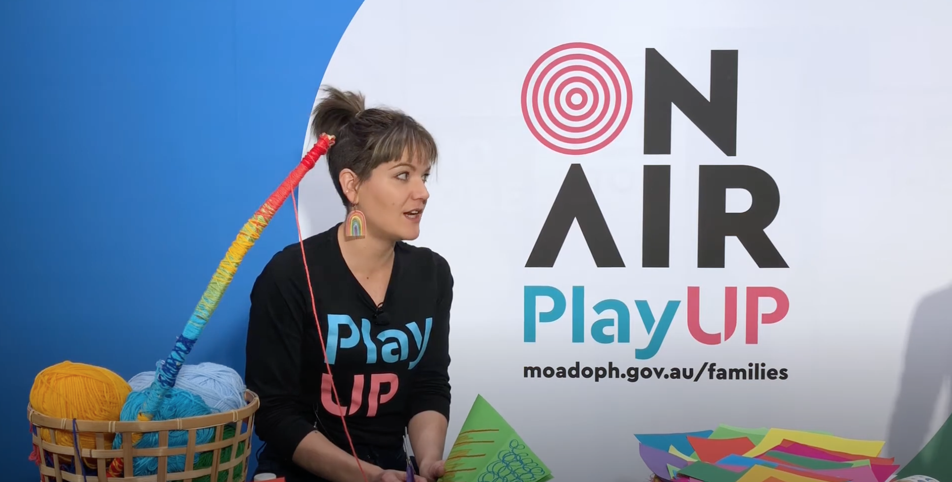 A PlayUP facilitator stands behind a table covered in craft supplies. 