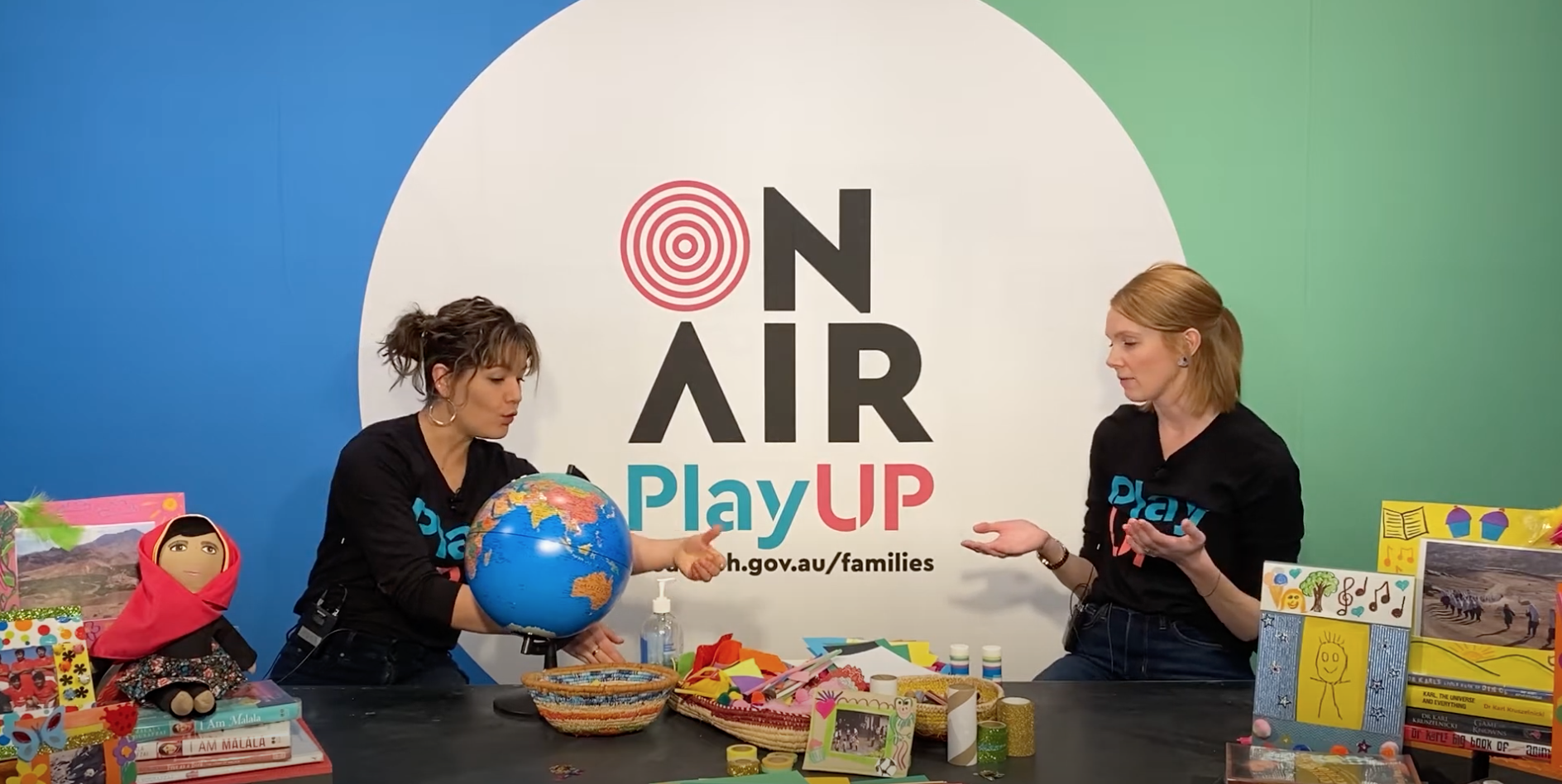 Two PlayUP facilitators stand behind a table with craft supplies. 