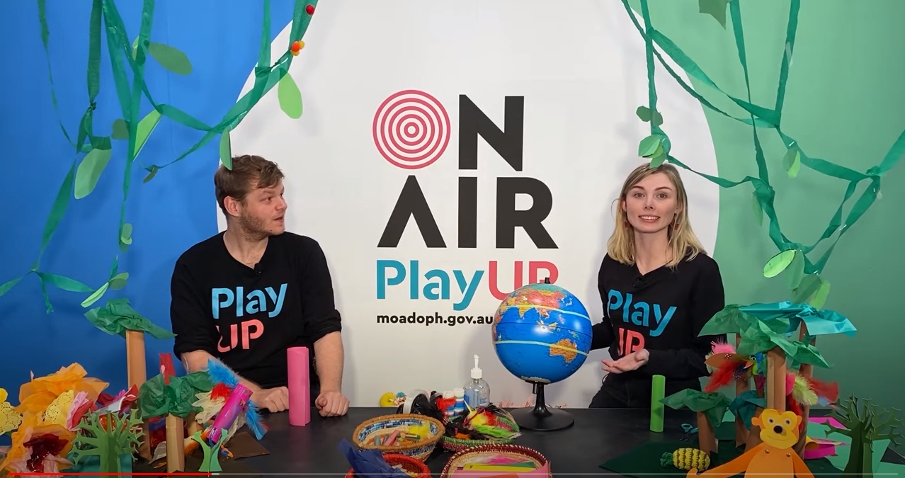 Two facilitators wearing black shirts that say PlayUP make something out of cardboard.