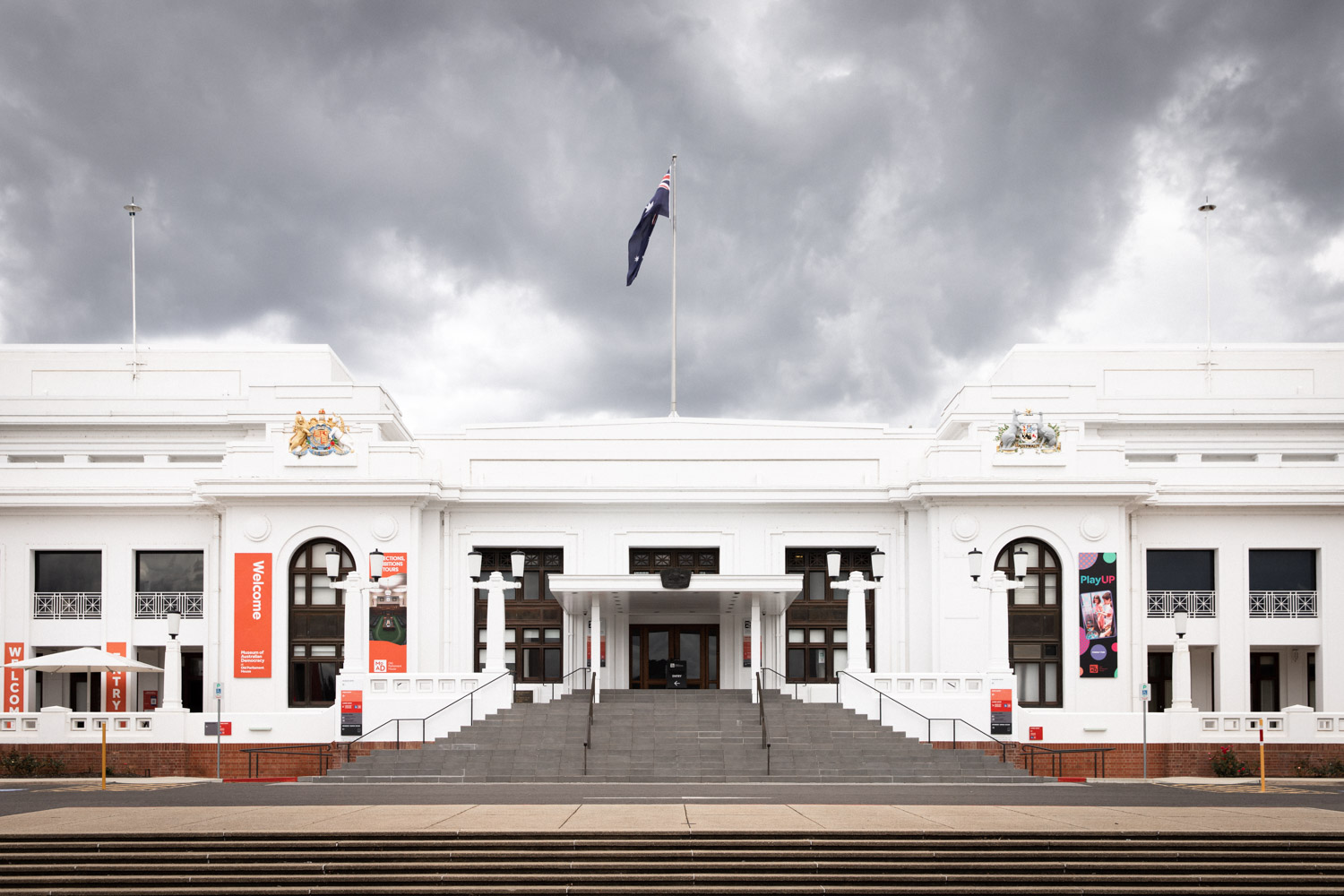 A large staircase leads up to a white old building with a flag on the top.