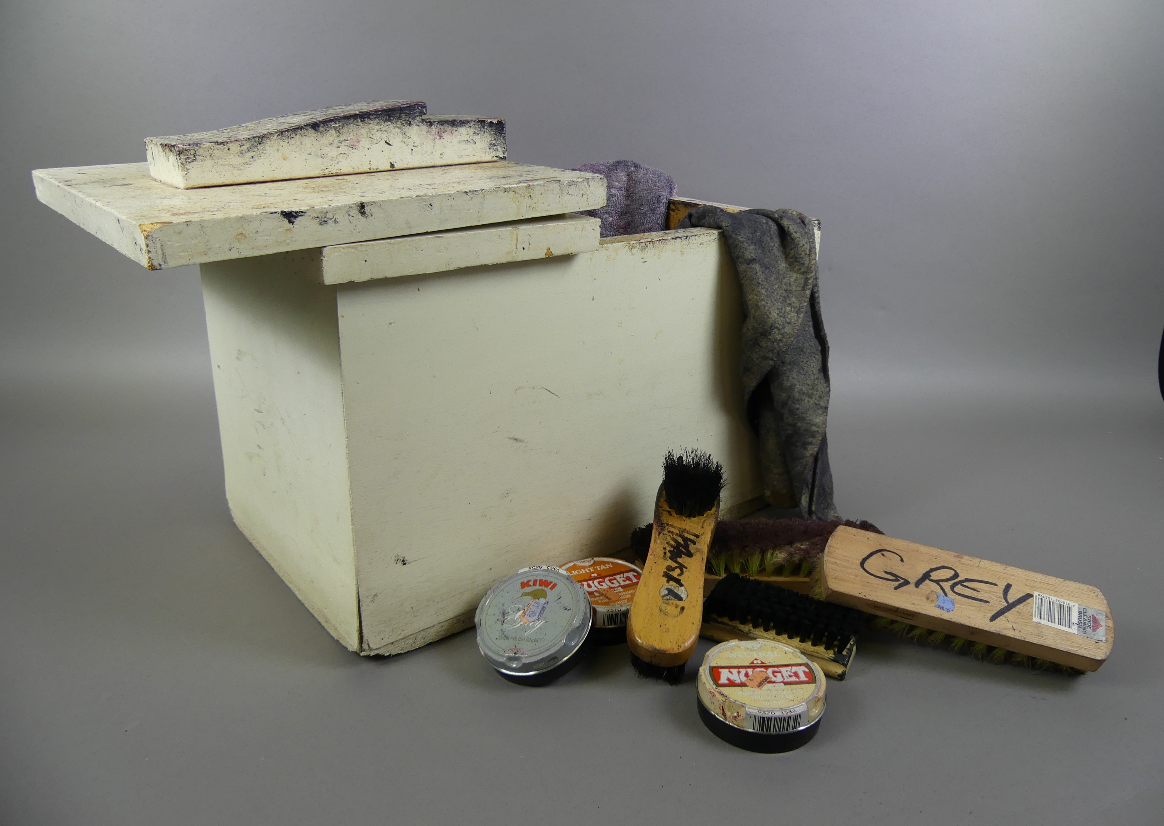 A solid wooden box containing dirty cloths, four shoe brushes and three tins of shoe polish.