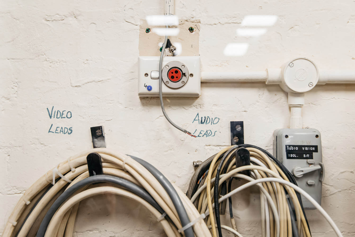 Piles of phone cables in loops hung on a wall with the words video leads and audio leads above them in texta.