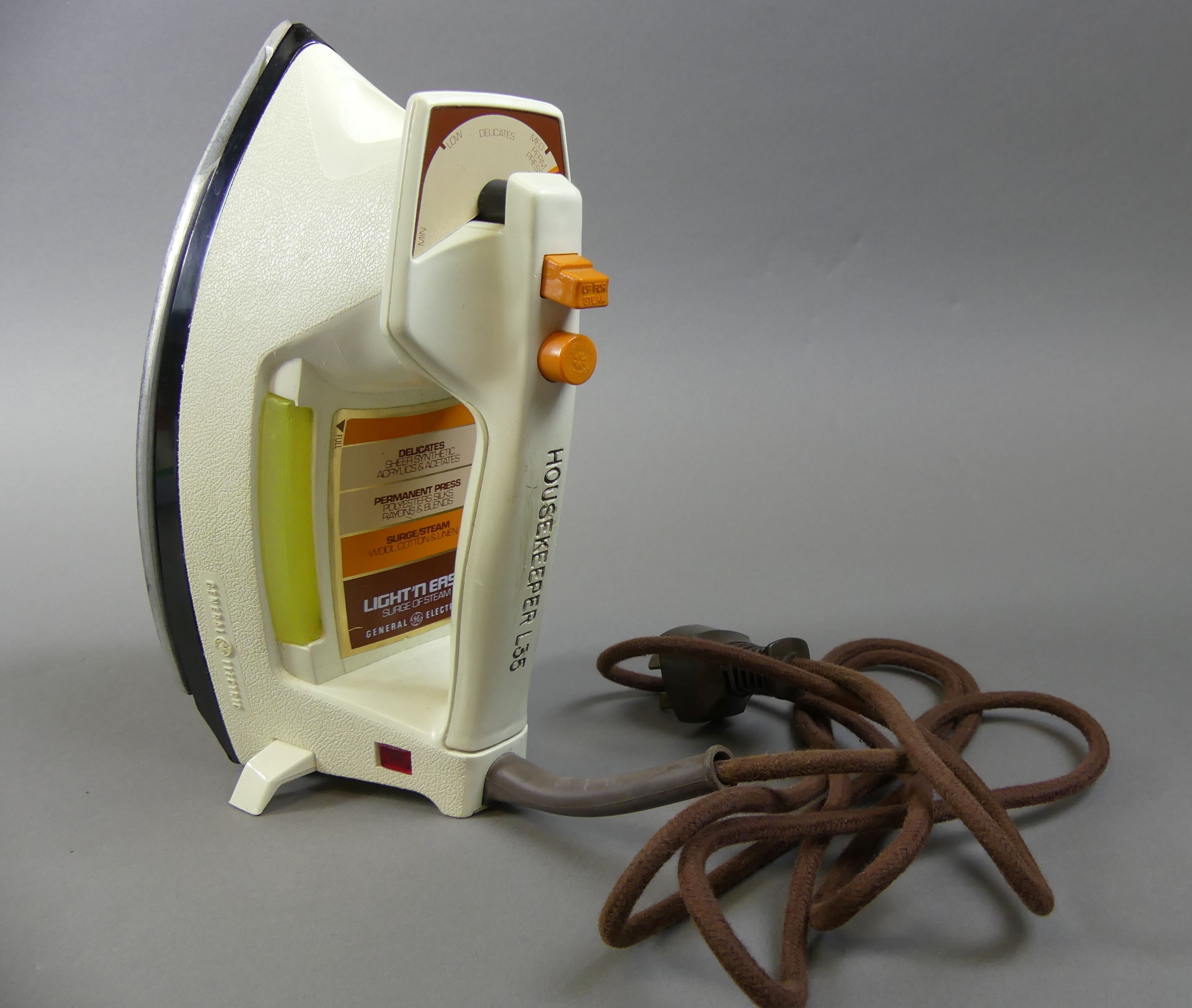 A white hand iron with orange buttons and a brown power cord.