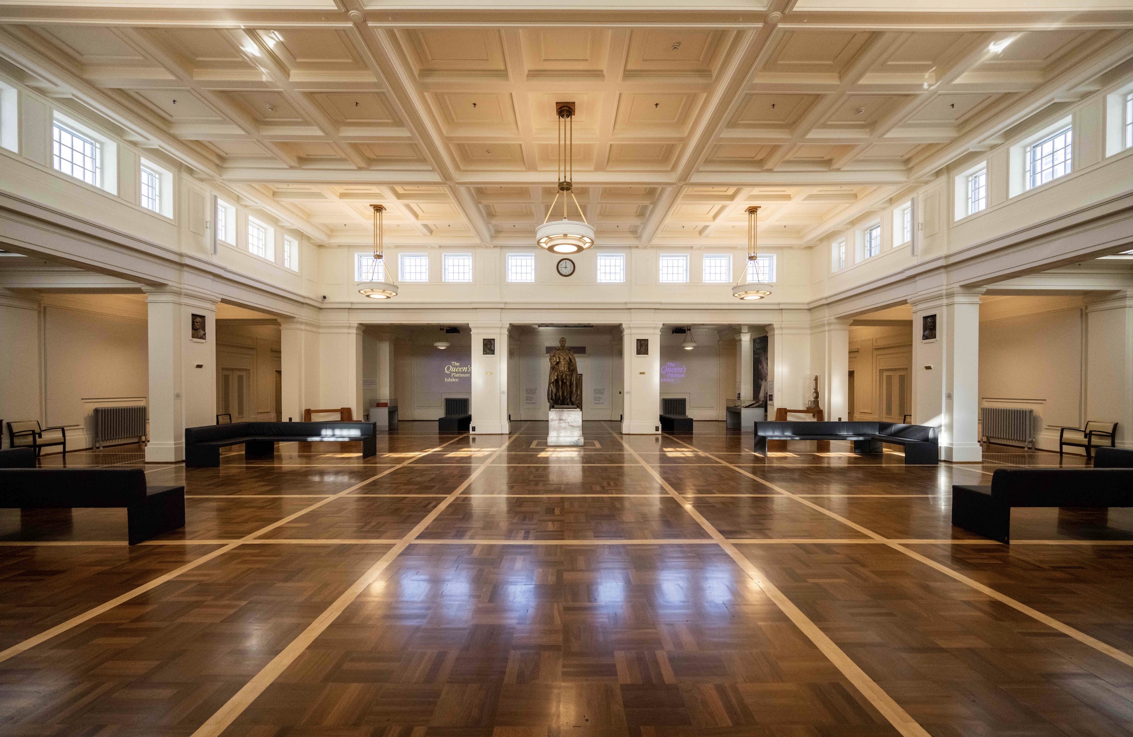 A bronze statue of a man is the focal point of a hall with a timbered floor and white columns.