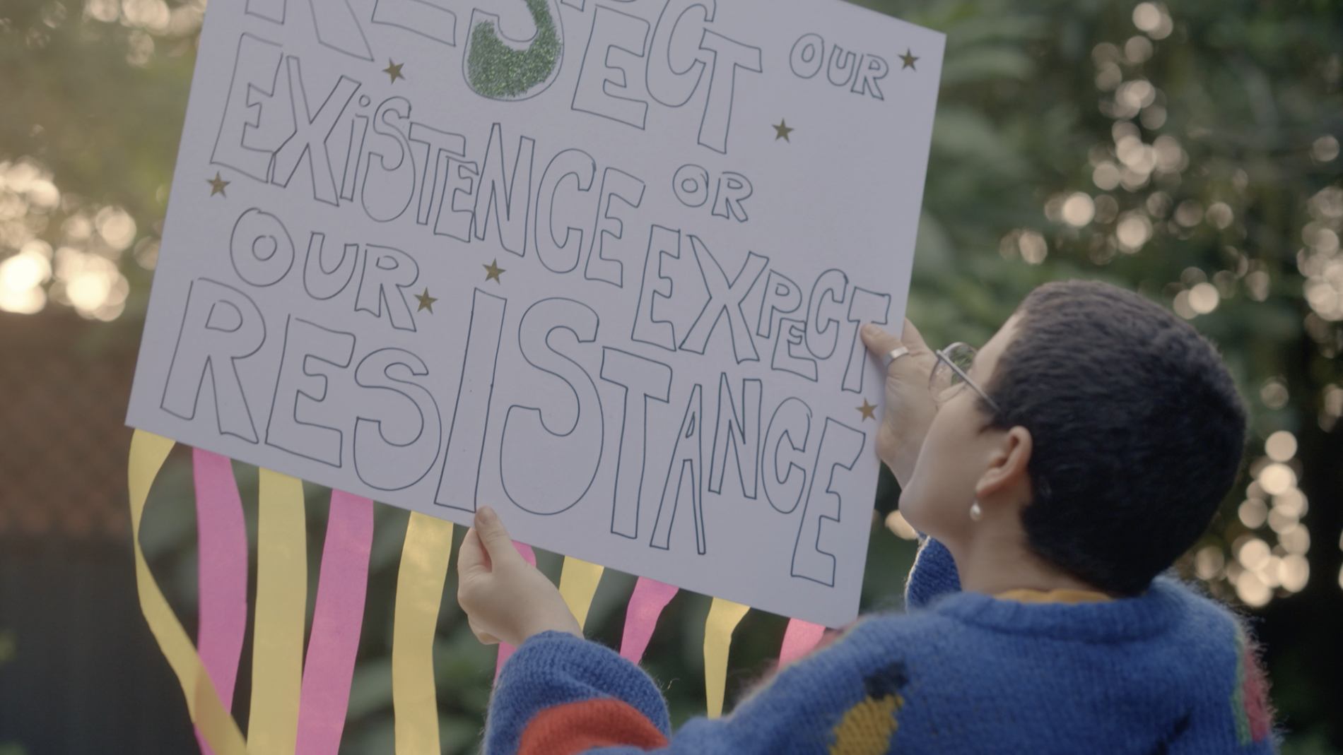 A person holds up a protest placard with the label "Respect our existence or expect our resistance"