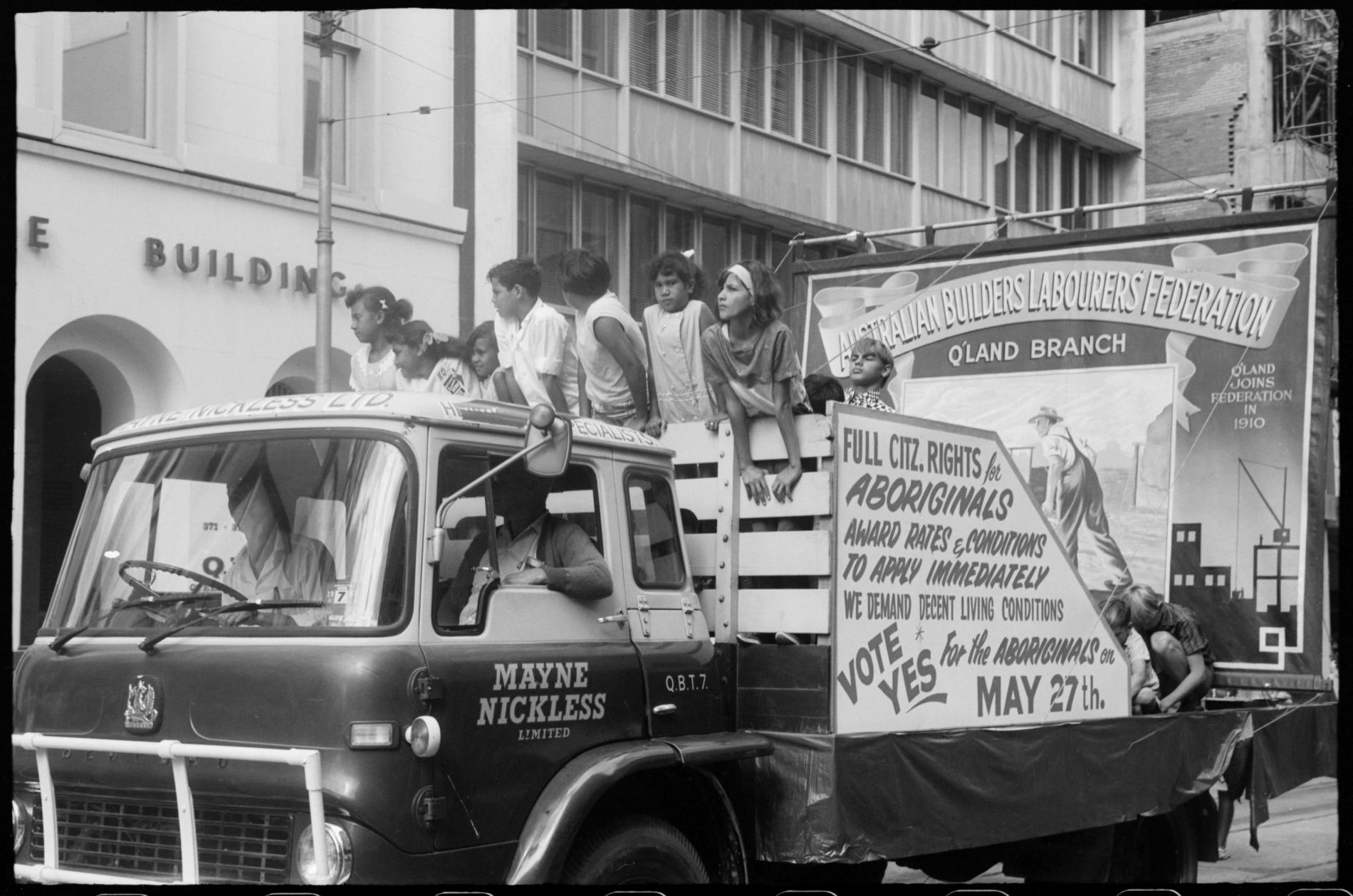 A black and white photo of a car and a float with a group of people standing in front of a sign that reads full citz rights for Aboriginals.