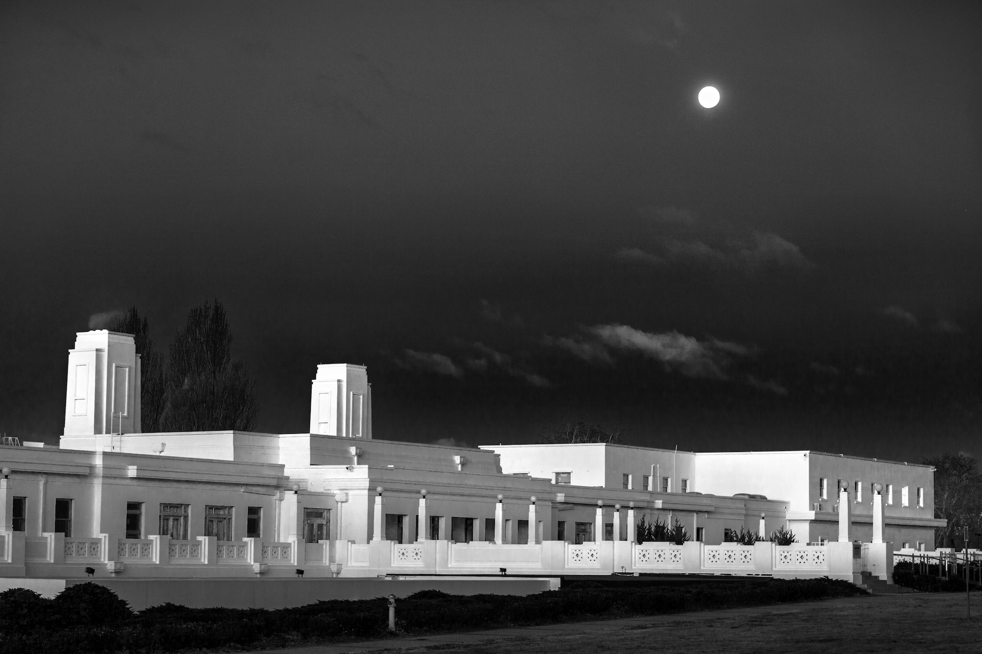 A long white building, Old Parliament House, with a dark sky and the moon in the background. A long white building, Old Parliament House, with a dark sky and the moon in the background.