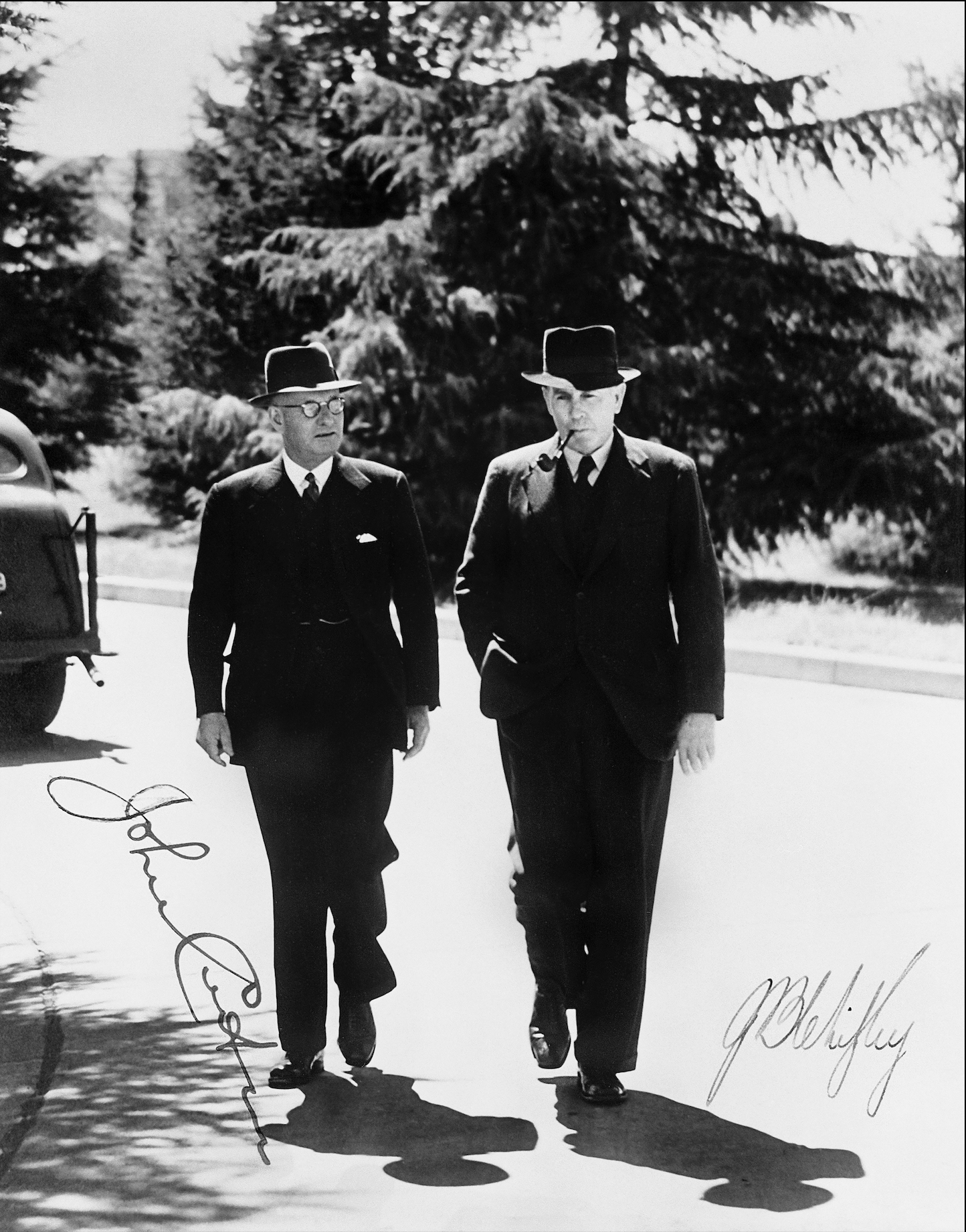 A black and white photo of two men in dark suits, wearing hats, one with glasses and the other with a pipe in his mouth walking. There are two signatures on the photo. One reads John Curtin, the other reads Ben Chifley. A black and white photo of two men in dark suits, wearing hats, one with glasses and the other with a pipe in his mouth walking. There are two signatures on the photo. One reads John Curtin, the other reads Ben Chifley.