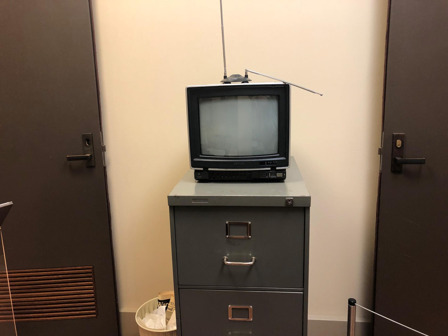 A small television with an aerial antenna sits on top of a grey filing cabinet.