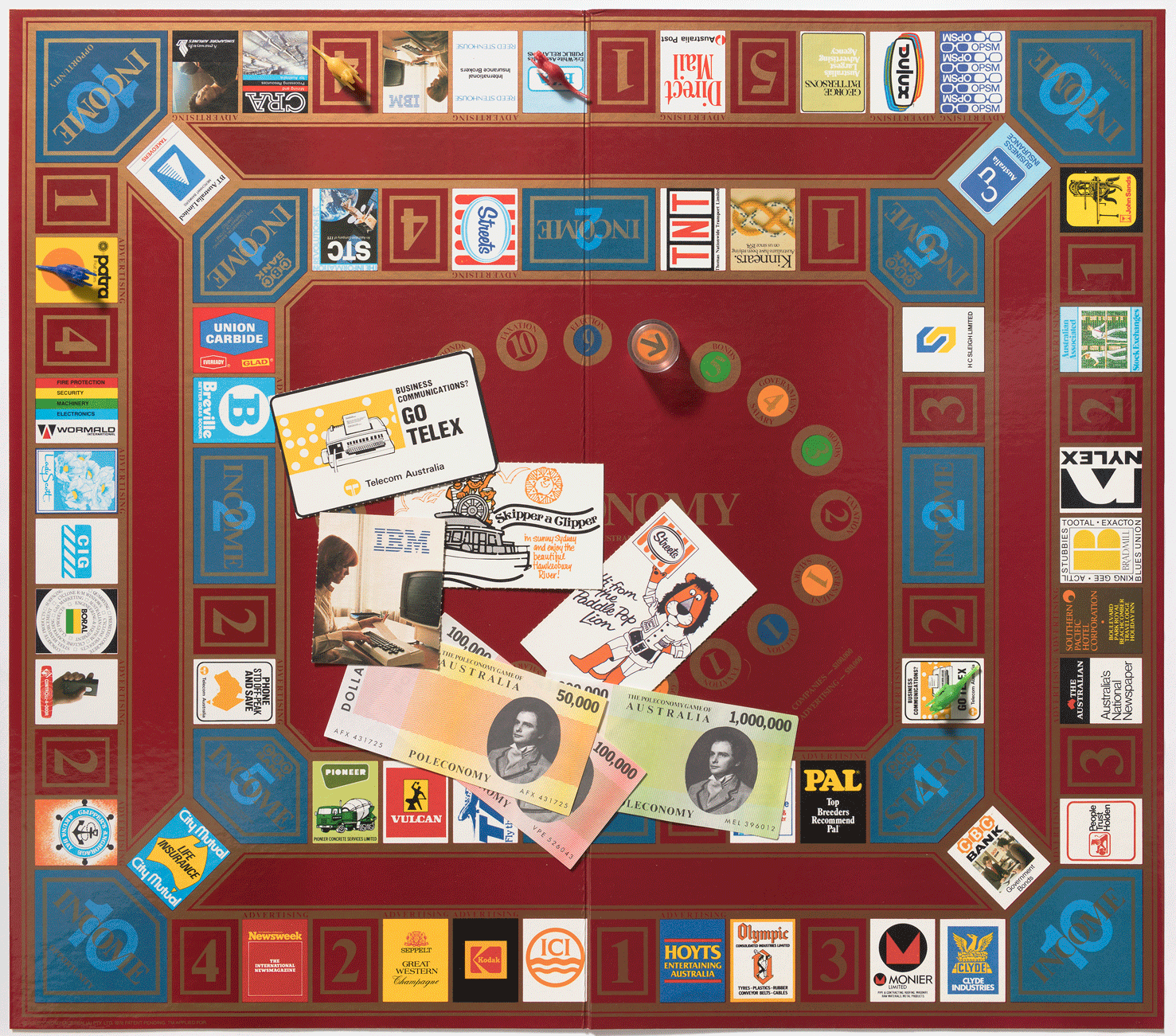 A board game with a dark red board opened up with a row squares around the outside of the board with the names of different companies such as Kodak, Hoyts and Newsweek. In the centre are some game pieces including 3 pieces of paper representing money and some cards with businesses on them including IBM and Telecom. 