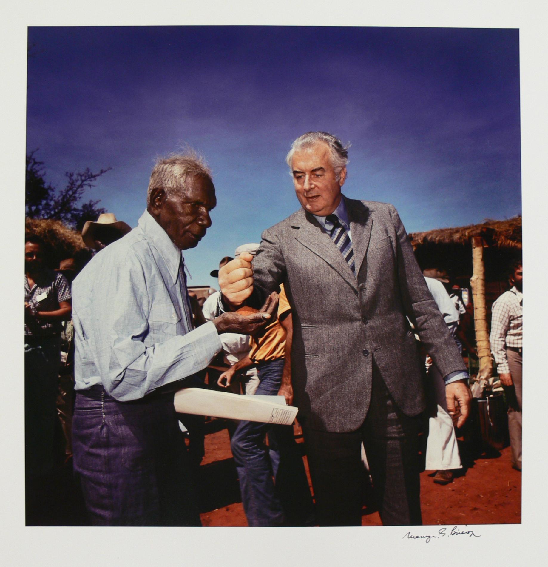 Prime Minister Gough Whitlam pouring earth through Vincent Lingiari’s hand while people look on.