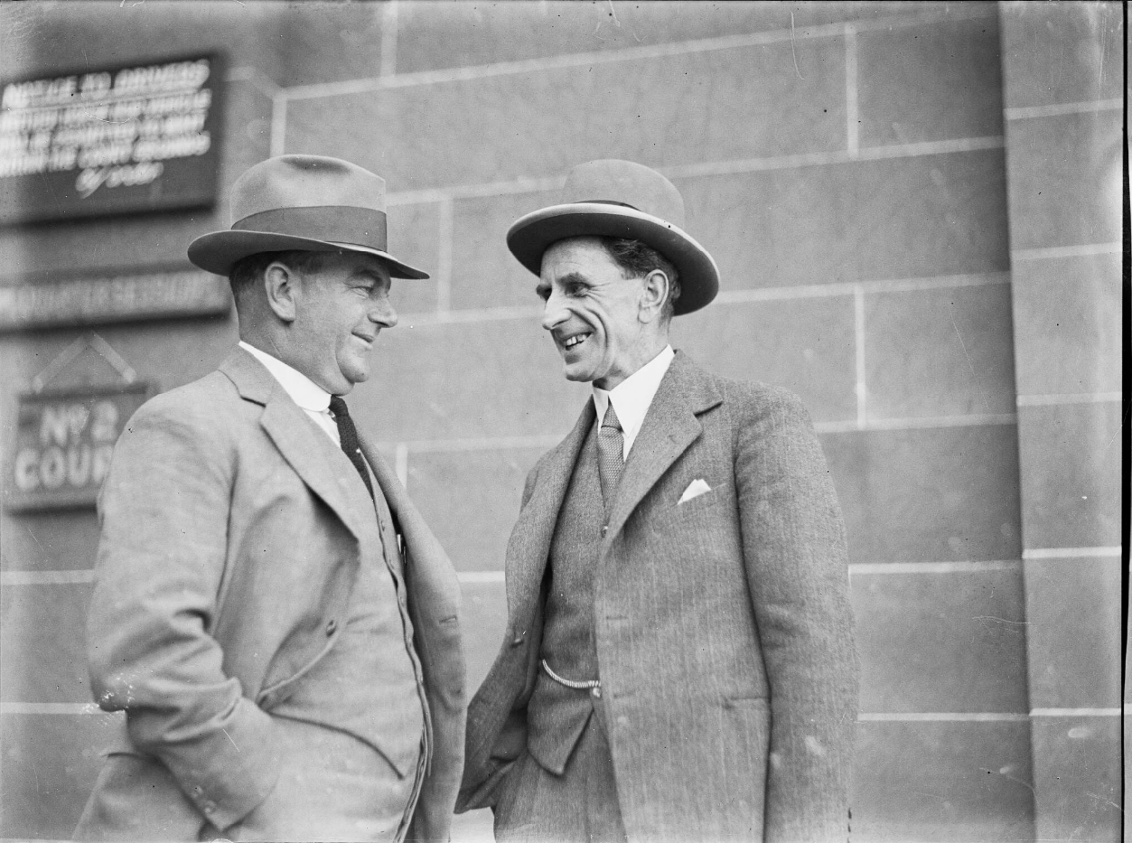 Donald Grant (on the right) smiling and speaking with another man, both wearing wide-brimmed hats and three-piece suits.