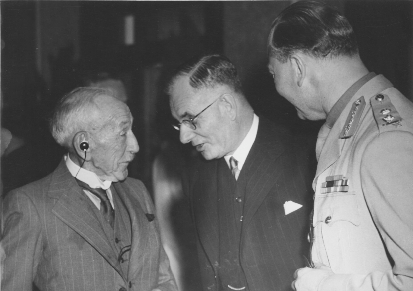 Billy Hughes wearing his 'accousticon', in conversation with John Curtin and the Duke of Gloucester.