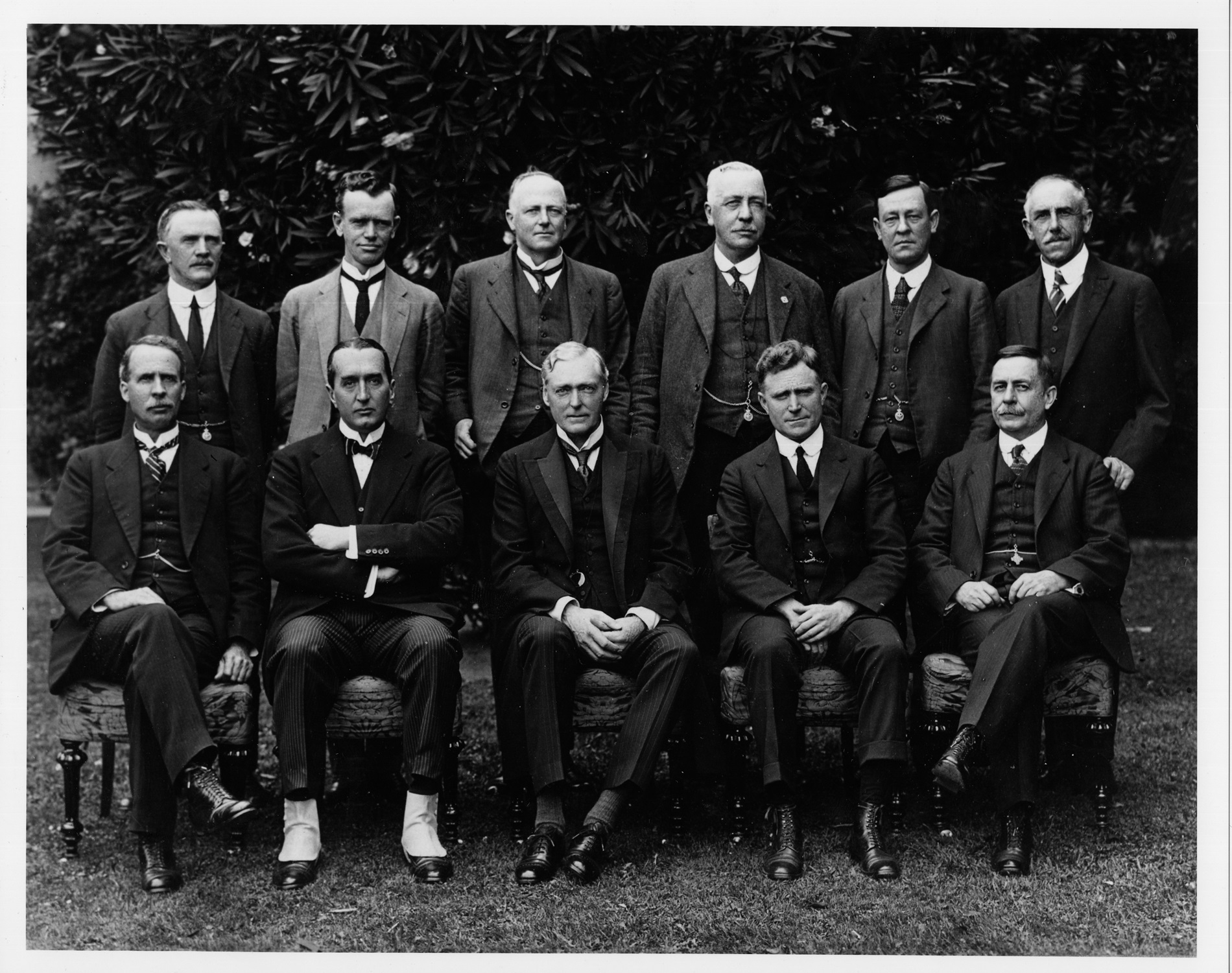 Black and white photograph of eleven men, posing in two rows, all wearing three-piece suits.