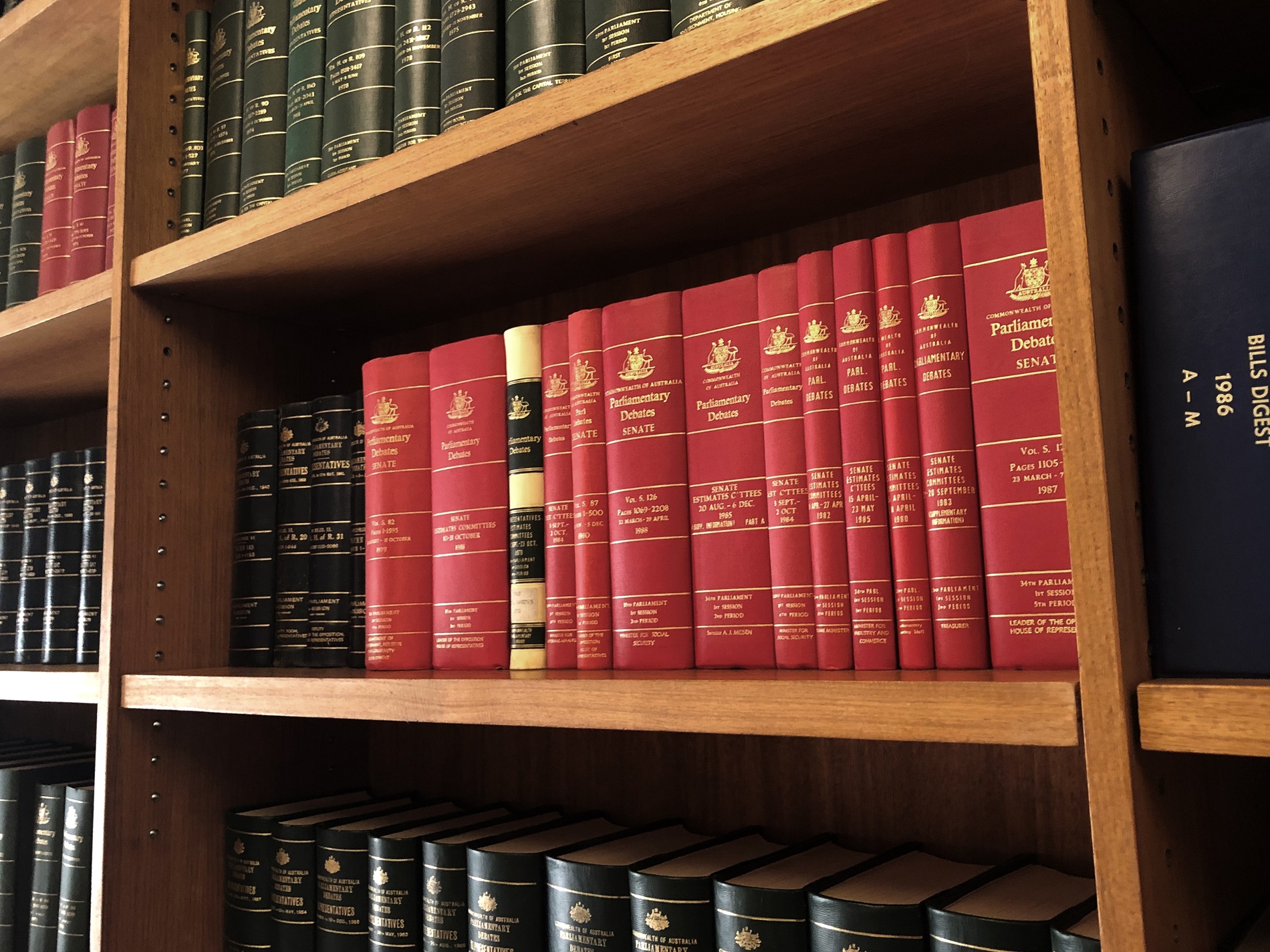 A row of red bound volumes on a shelf containing the proceedings of Senate Estimate committee hearings.