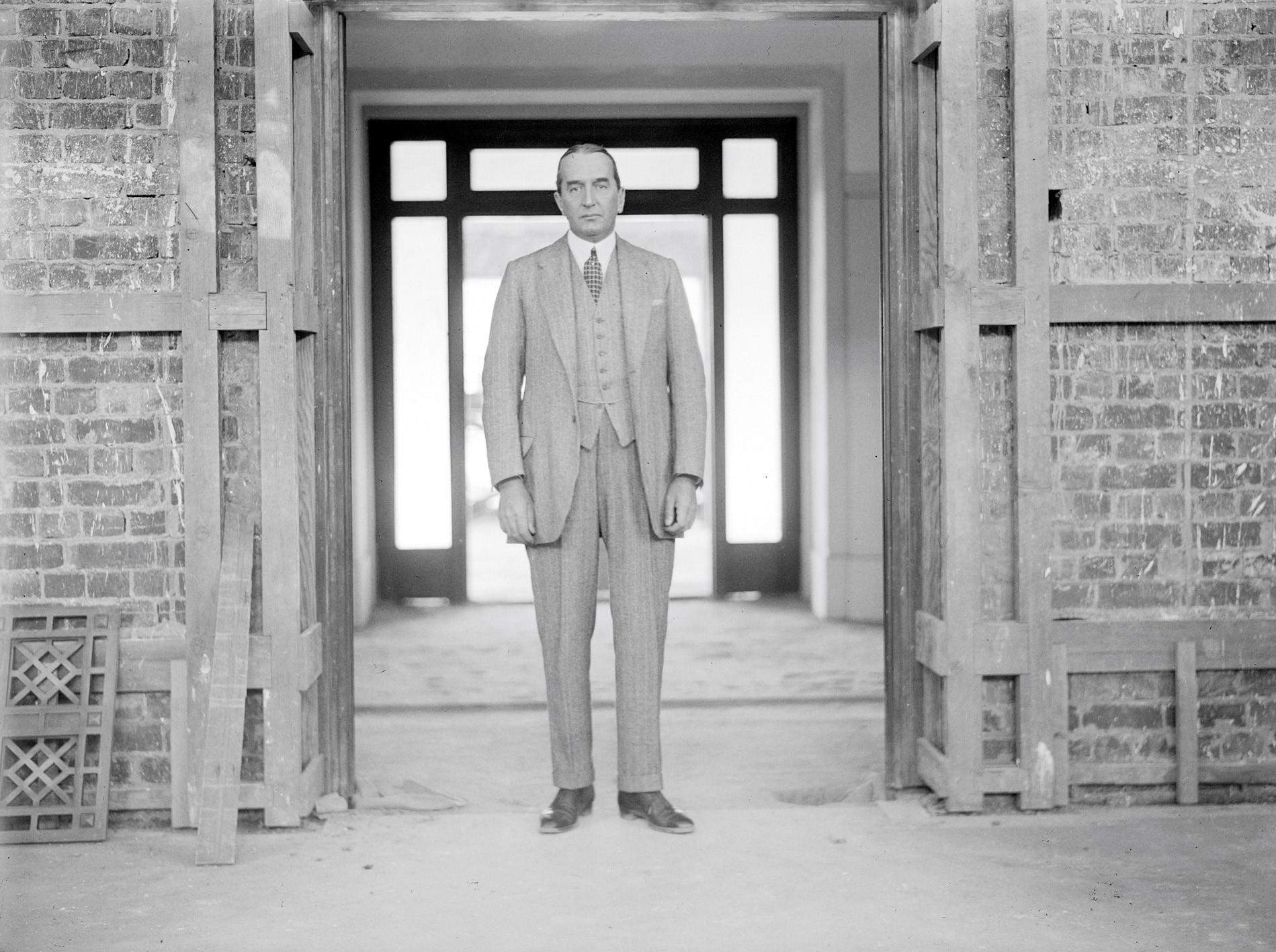 Black and white photograph of Stanley Bruce, wearing a three-piece suit, standing in a doorway at the construction site of Old Parliament House.