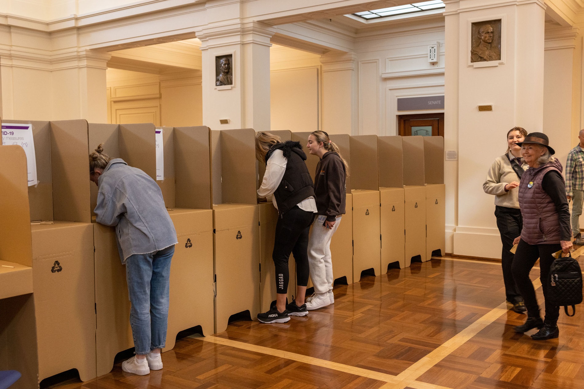 Three women standing at cardboard polling booths in King's Hall. 