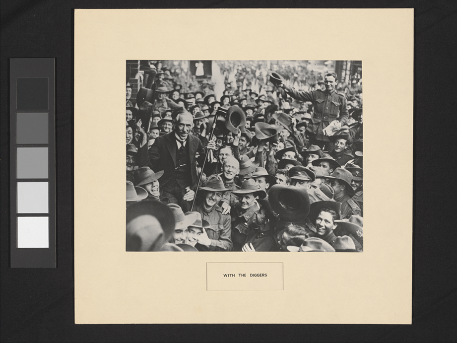 Prime Minister Hughes being held up by a crowd of returning soldiers in a busy street.