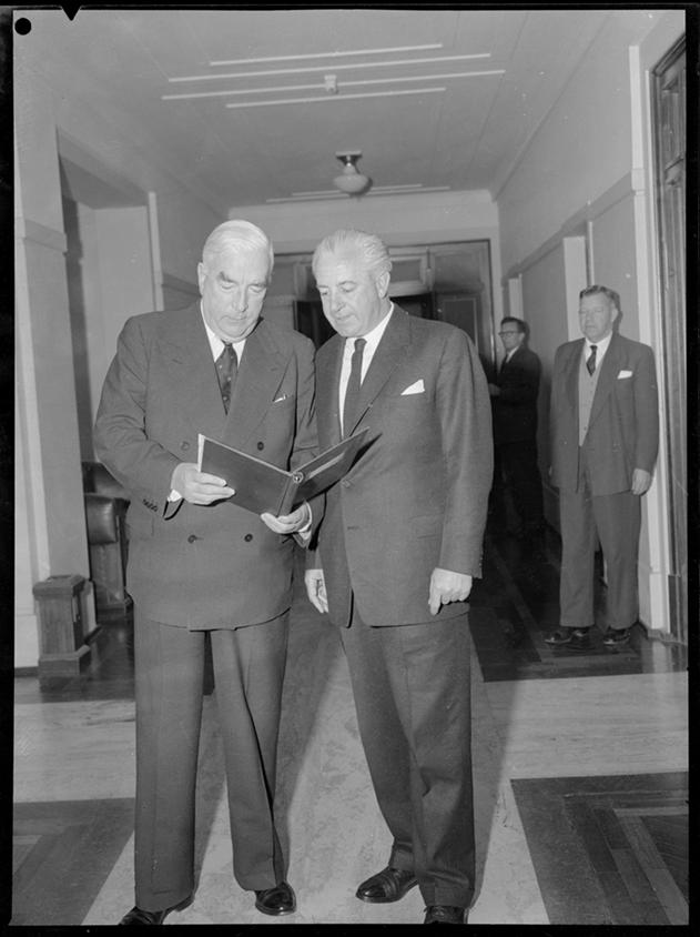 Prime Minister Menzies is holding a document, which both he and Harold Holt are looking at.