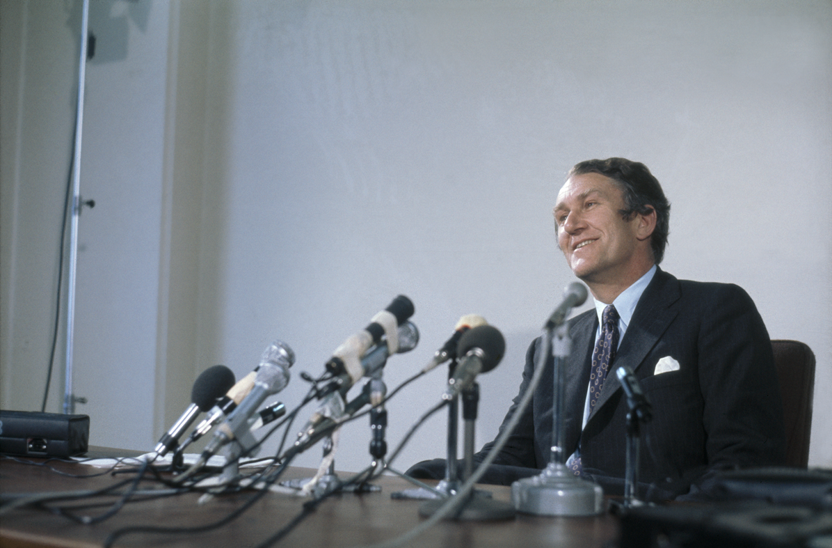 Malcolm Fraser looks out from behind a desk with microphones on it.