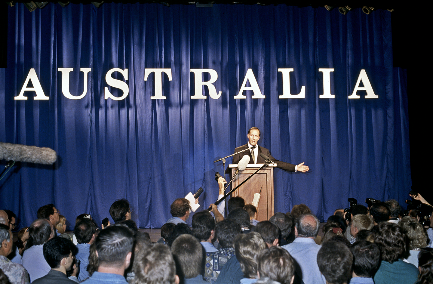 Paul Keating stands at a lecturn with the word 'Australia' behind him. A crows 