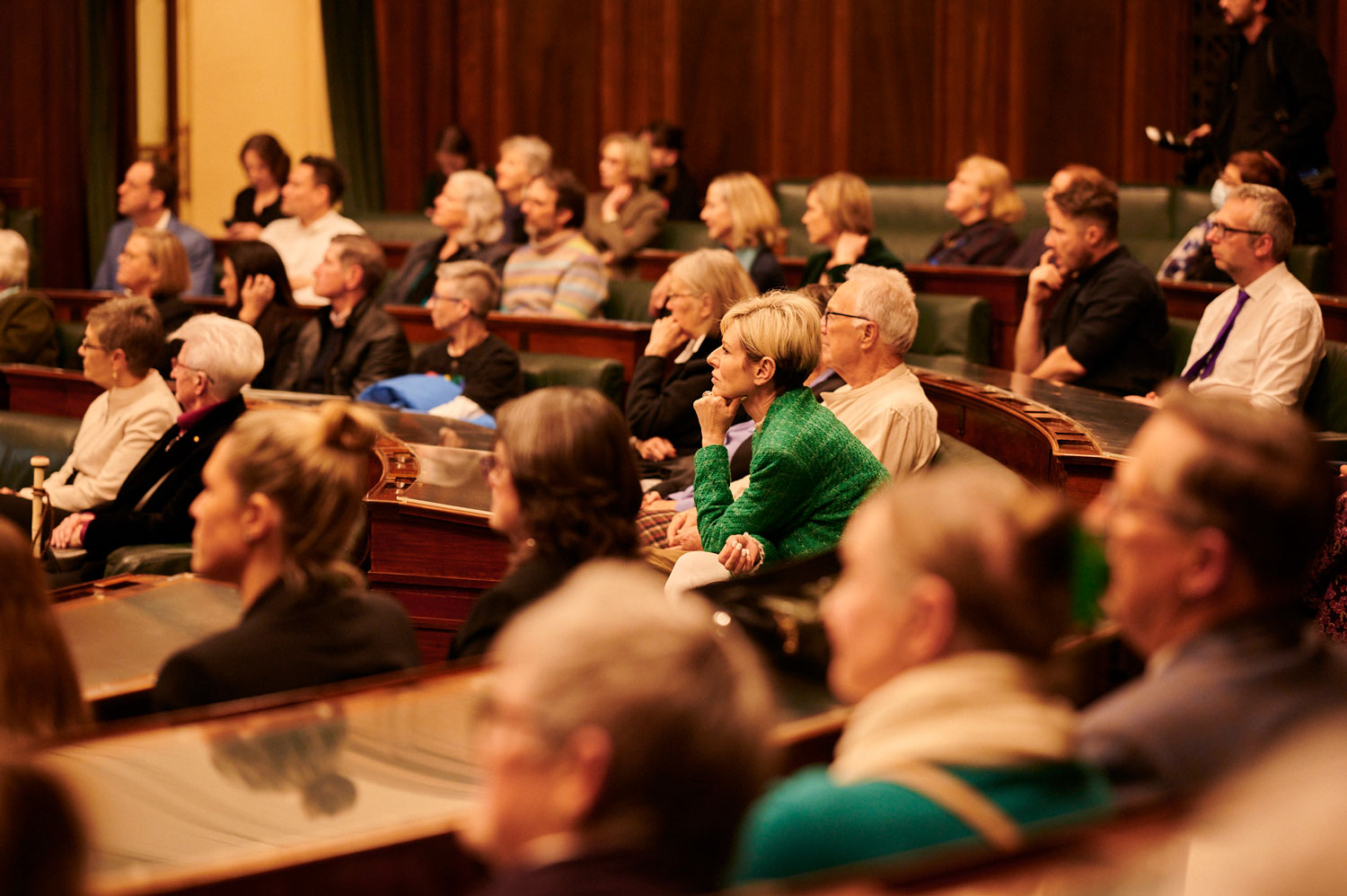 An audience sits on green leather benches in the House of Representatives at Old Parliament House. The room has wood panelled walls. An audience sits on green leather benches in the House of Representatives at Old Parliament House. The room has wood panelled walls.