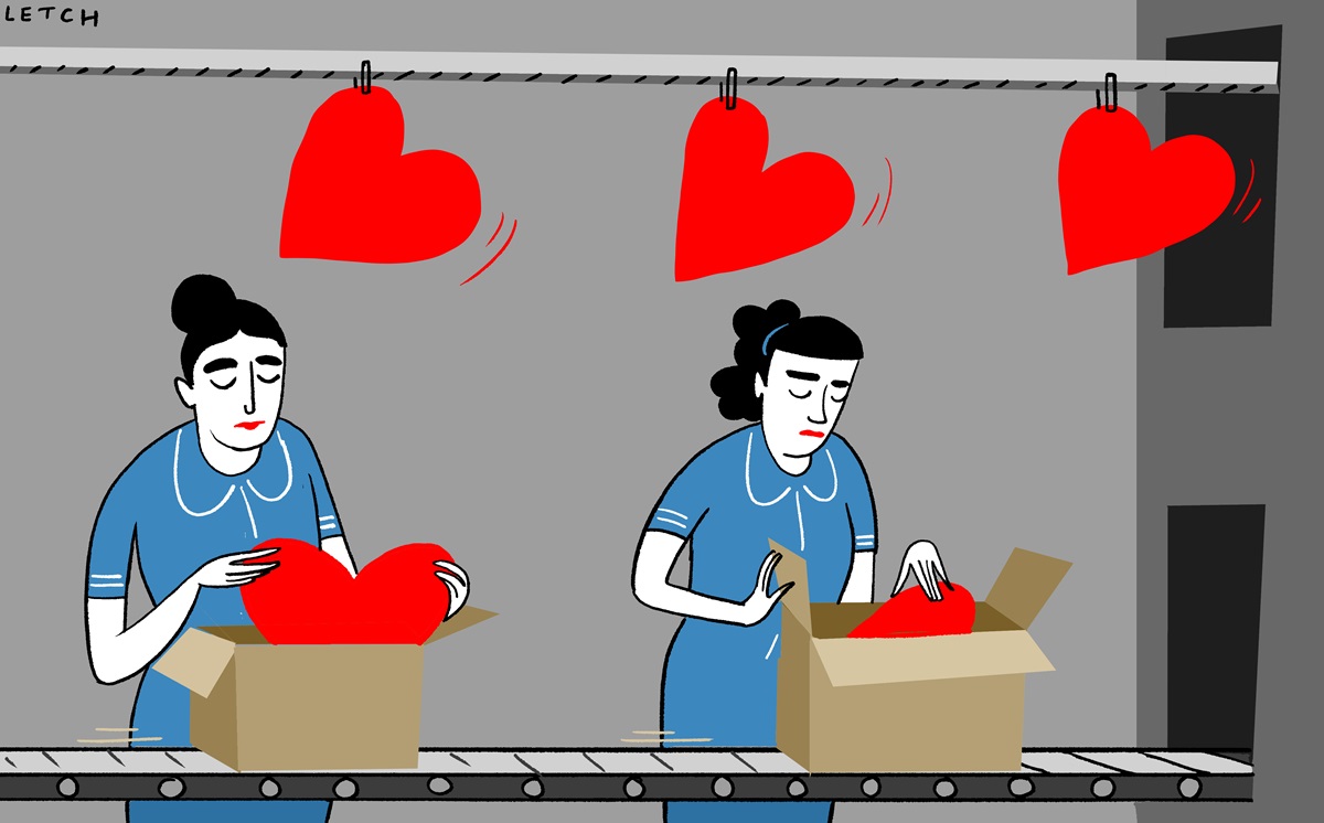 Two women in blue uniforms on a production line pack red hearts into cardboard boxes.