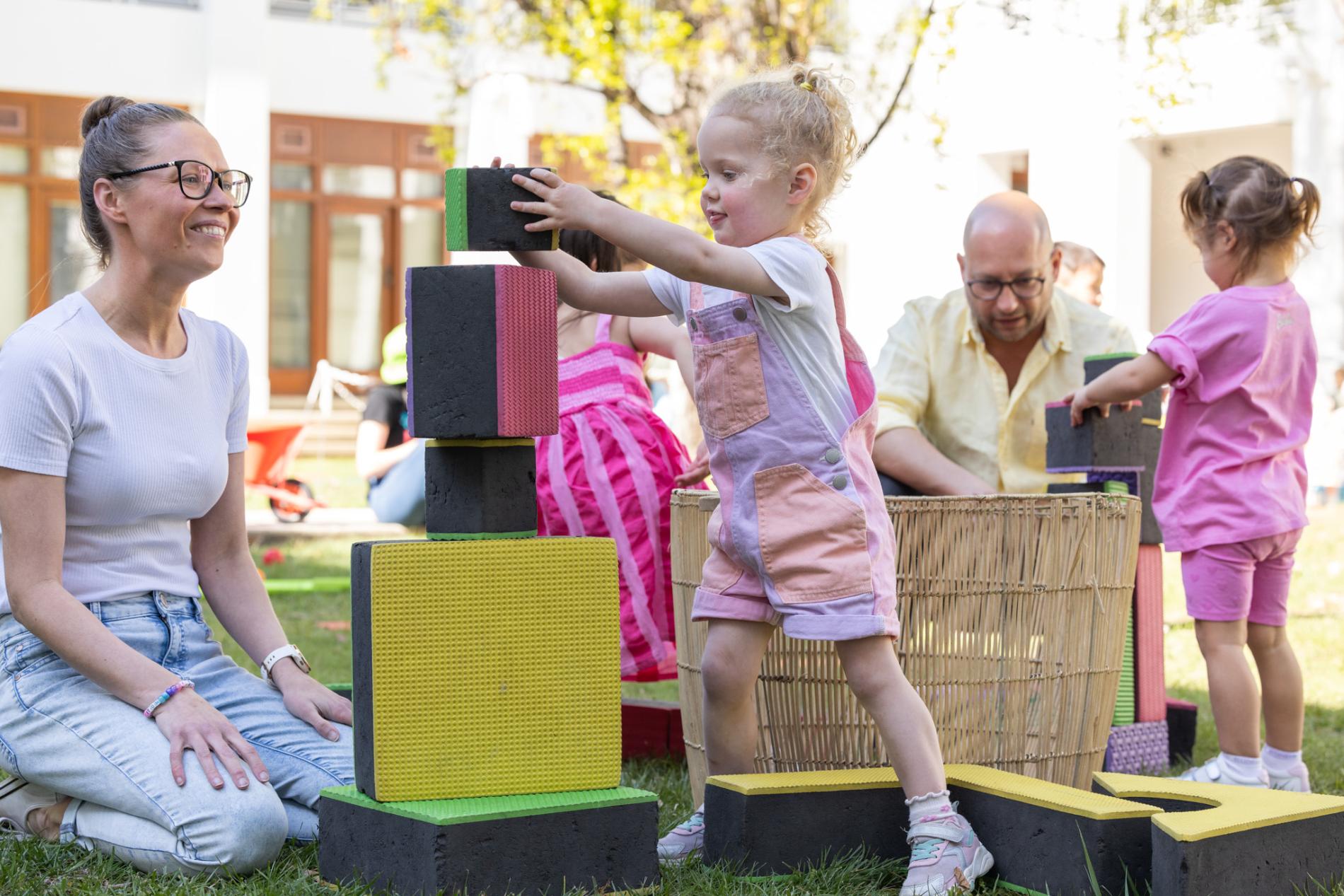 Kids and their parents play with large colourful blocks on the grass of the Old Parliament House courtyard.