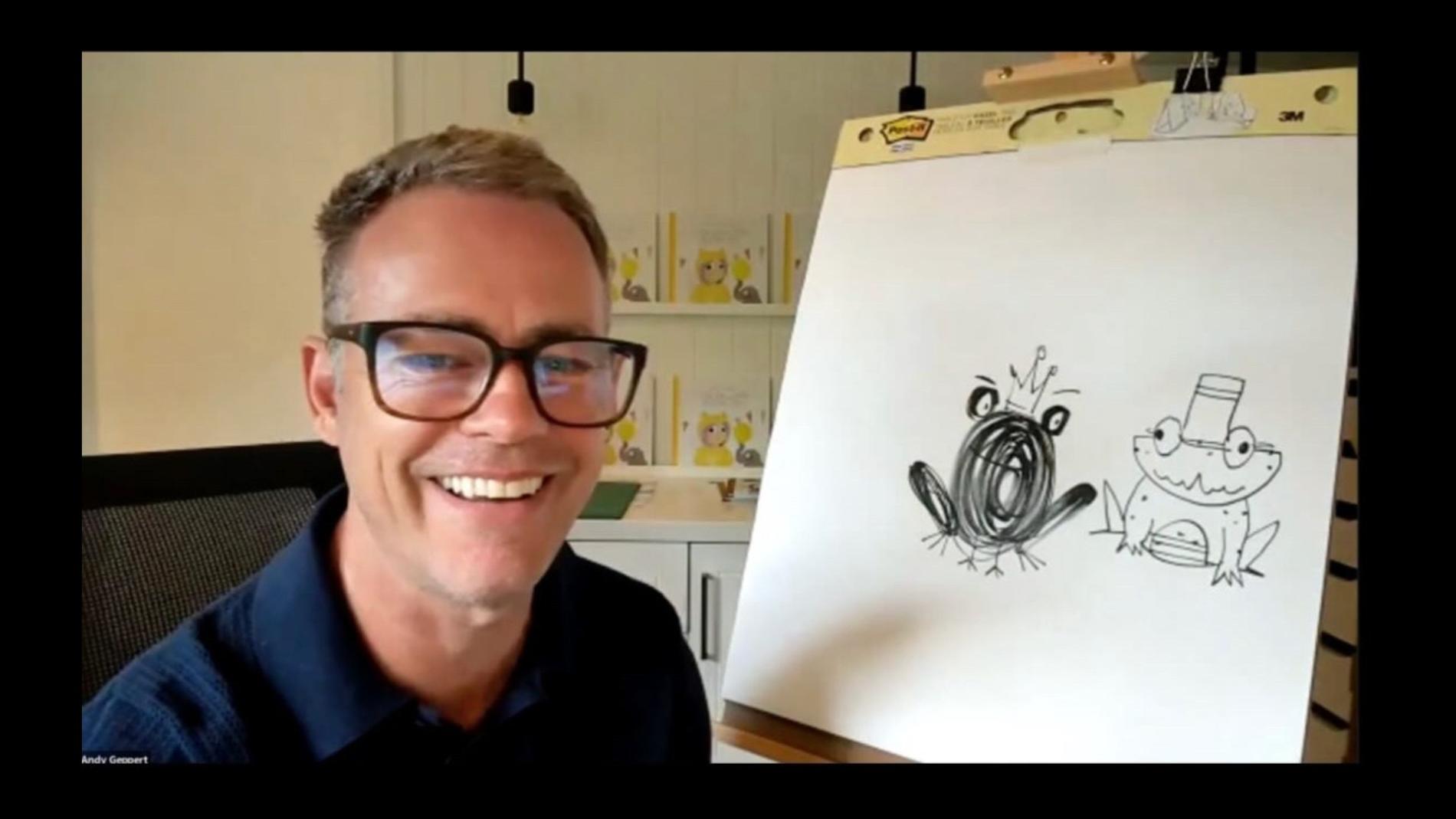 A man wearing glasses is smiling at the camera. There is a drawing next to him on an easel.