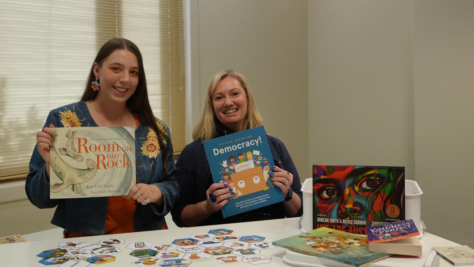 Two women hold up picture books in a room in Old Parliament House. Two women hold up picture books in a room in Old Parliament House.