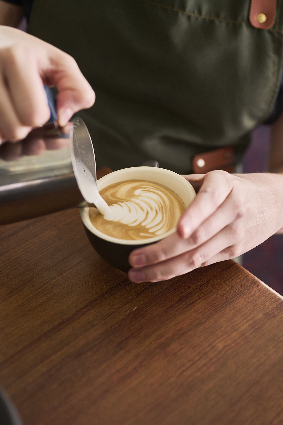 A barista using milk to create latte art on a coffee.
