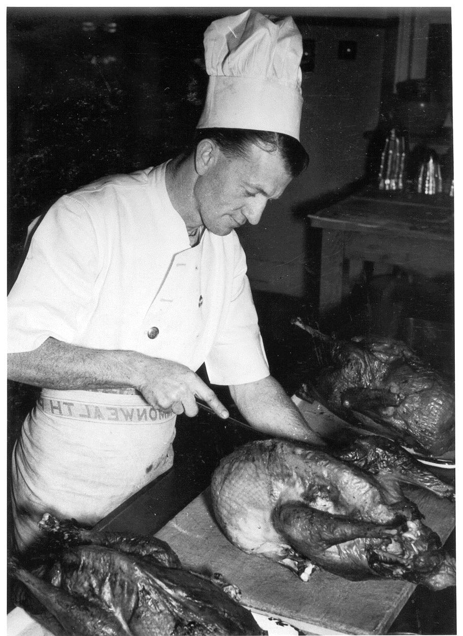 A chef in the kitchen cutting a rotisserie chicken.