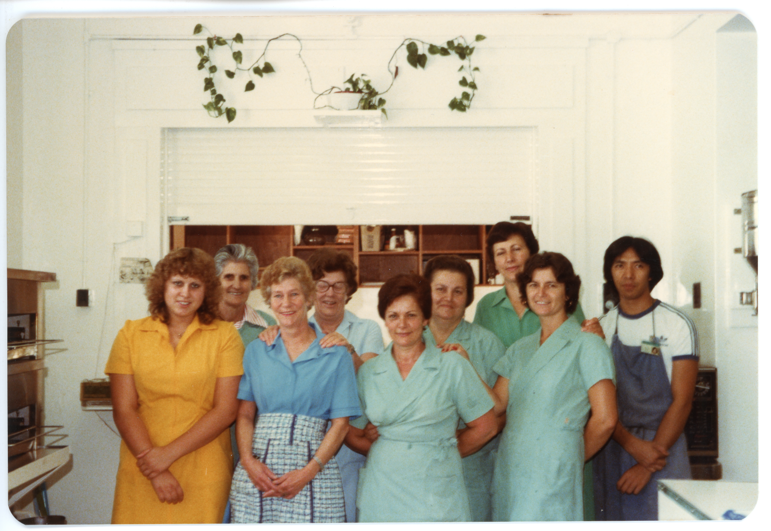 Kitchen staff wearing brightly coloured clothes, standing in a room smiling at the camera.