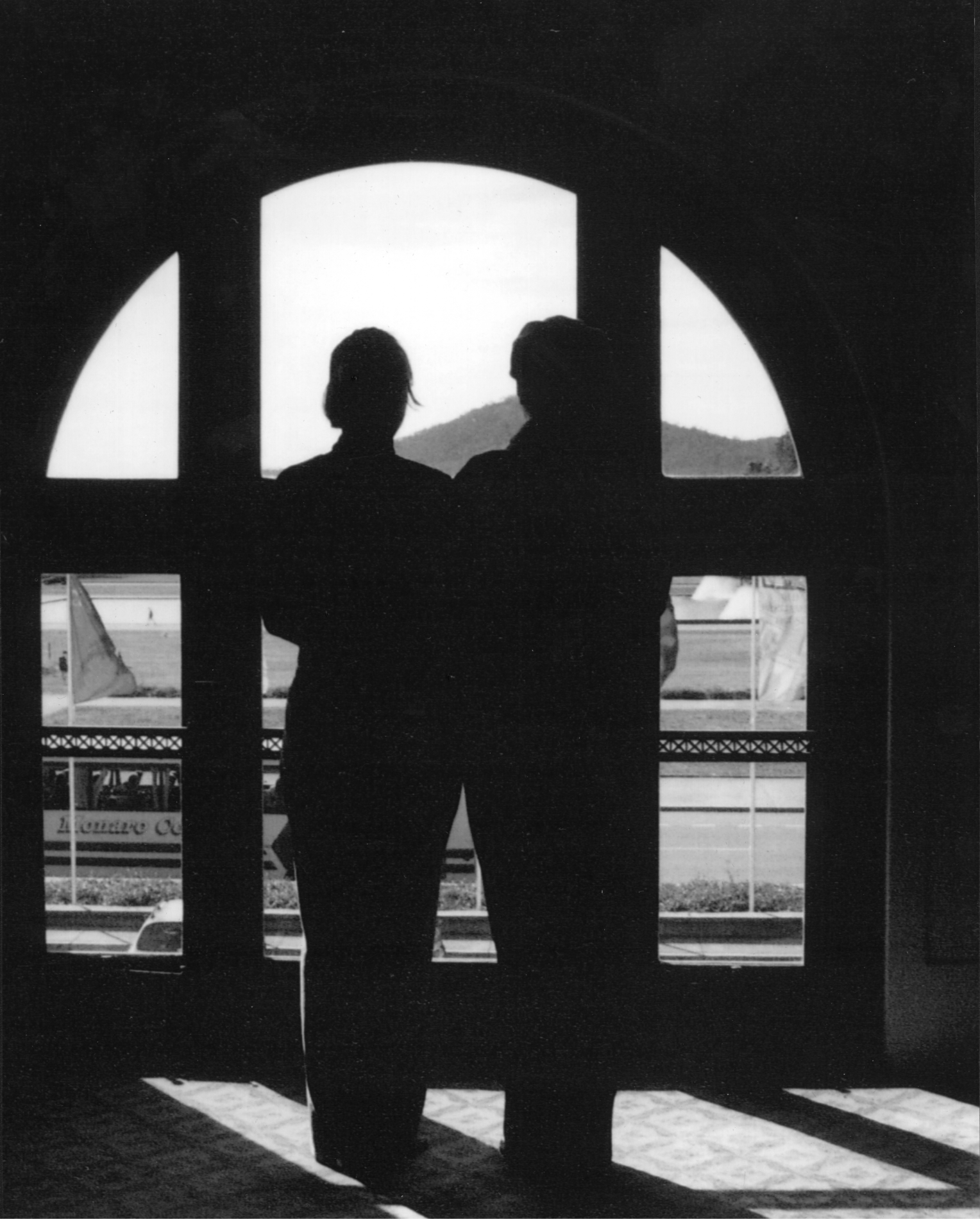 A silhouette of two people standing in a window at Old Parliament House, looking out towards Mount Ainslie.