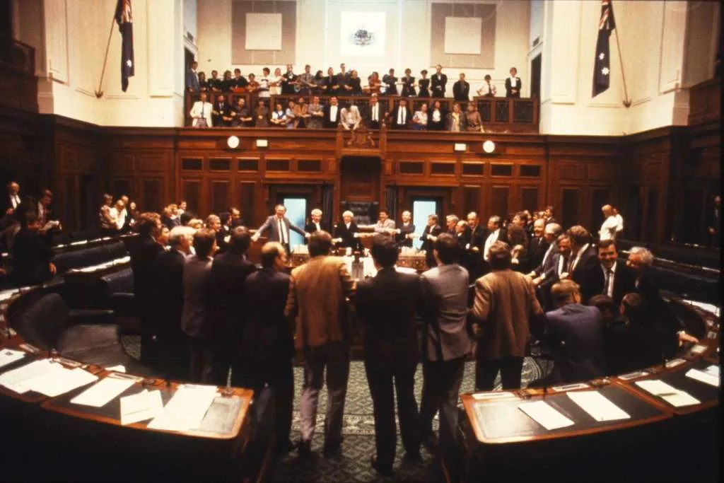 Groups of people stand in the House of Representatives Chamber with arms linked.
