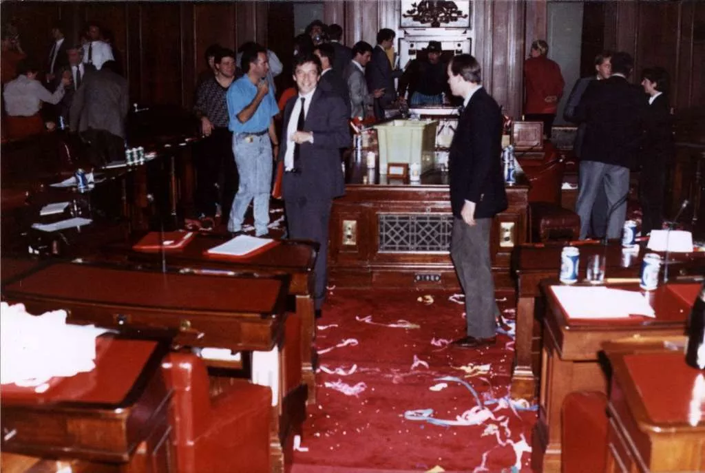 People mingle in the Senate chamber, with party decorations littered on the red carpet and beer cans sitting on the benches.