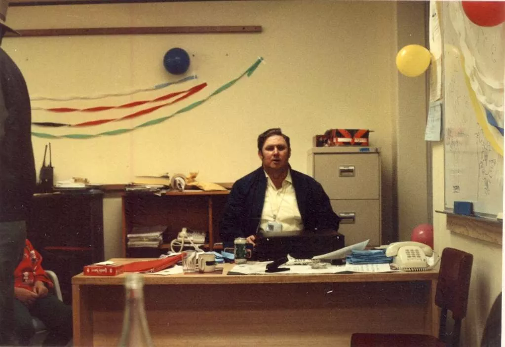Jim Douglass sits at a desk in an office decorated with balloons and streamers.
