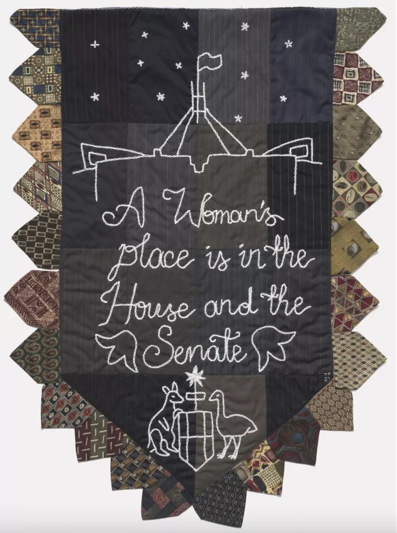 Black, grey and brown embroidered banner with the Australian coat of arms that says 'A woman's place is in the House and the Senate'.