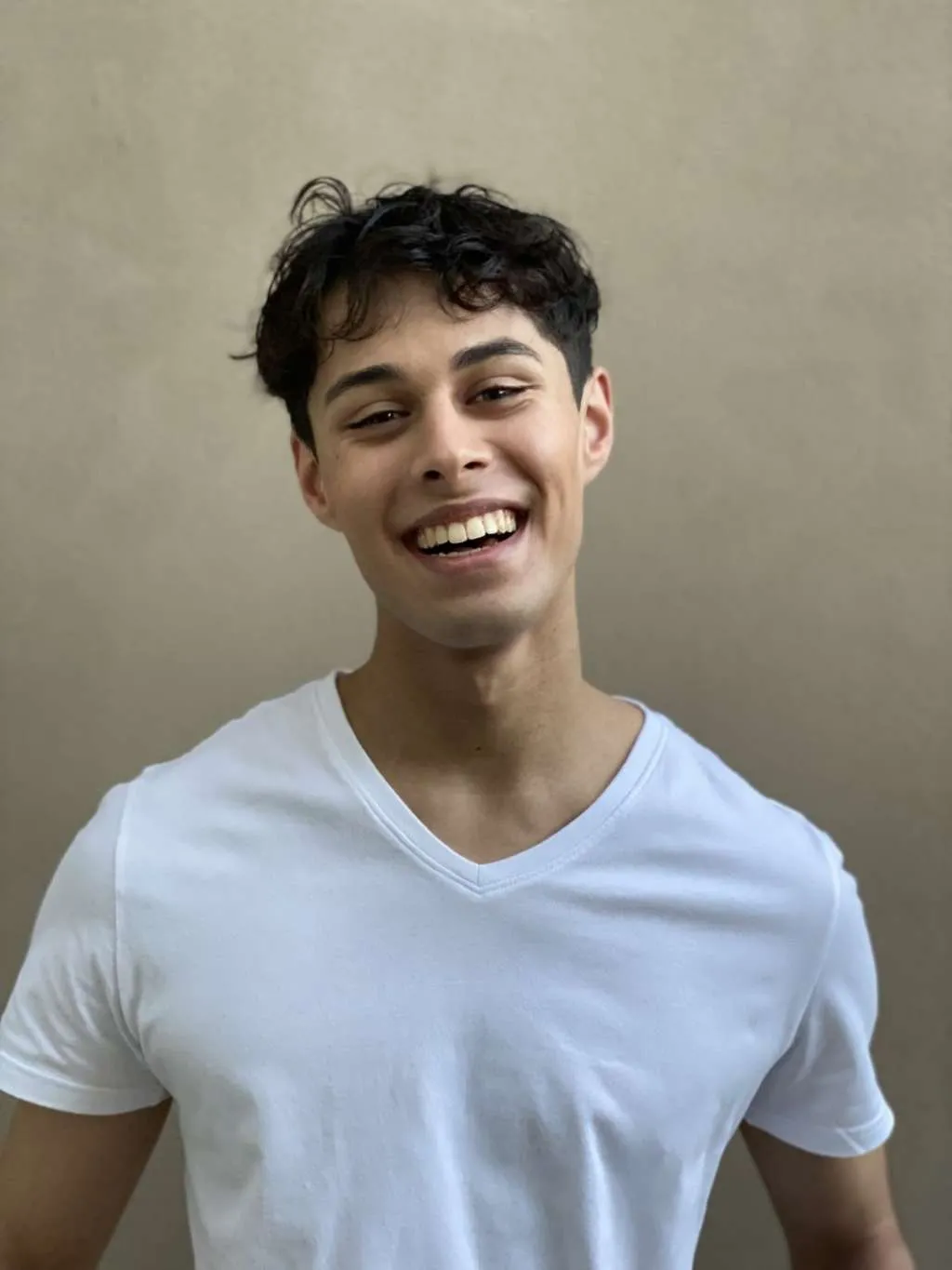 A young man, Ben Nowrojee, wearing a white t-shirt and smiling.