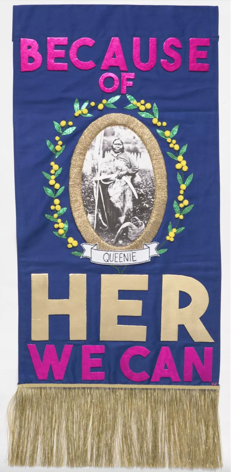Purple embroidered tapestry containing the words 'Because of her, we can', complete with a photo of First Nations woman Queenie.