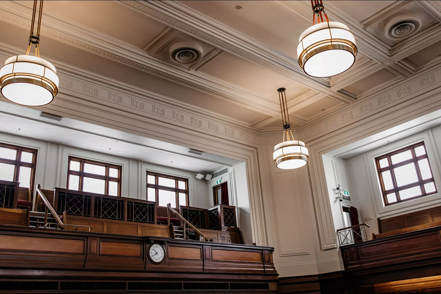 A close up of a white ceiling with ornate detailing, art-deco style pendant lighting and a timber gallery for the press to look down onto the floor of the House of Representatives.