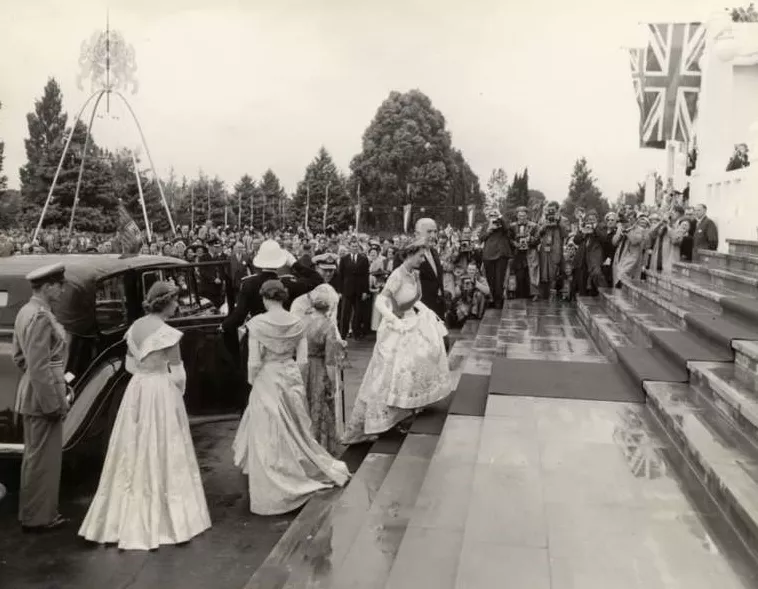 Queen Elizabeth walks up the stairs of Old Parliament House in 1954, wearing a formal gown and surrounded by people. 