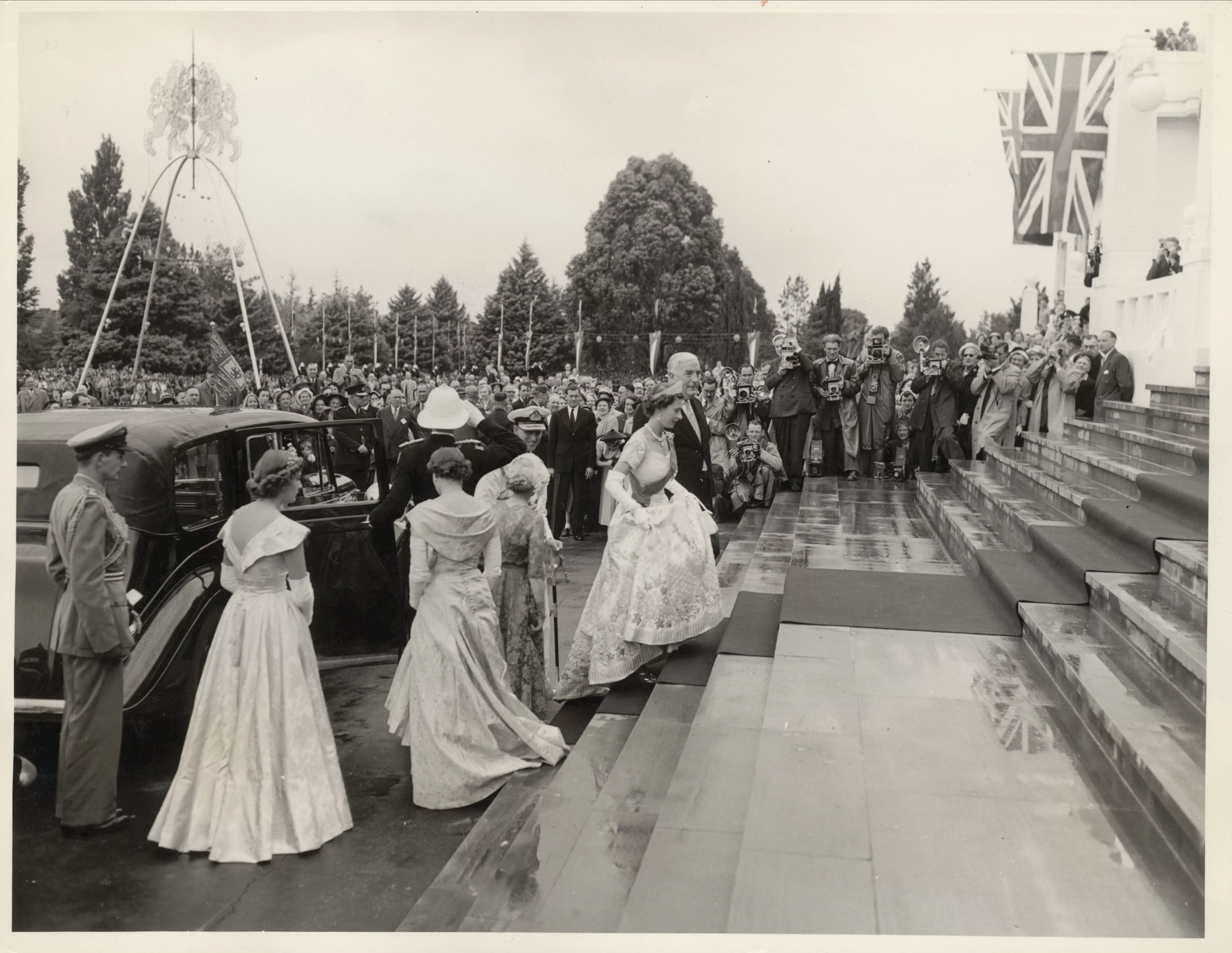 Queen Elizabeth walks up the stairs of Old Parliament House in 1954, wearing a formal gown and surrounded by people. Queen Elizabeth walks up the stairs of Old Parliament House in 1954, wearing a formal gown and surrounded by people.