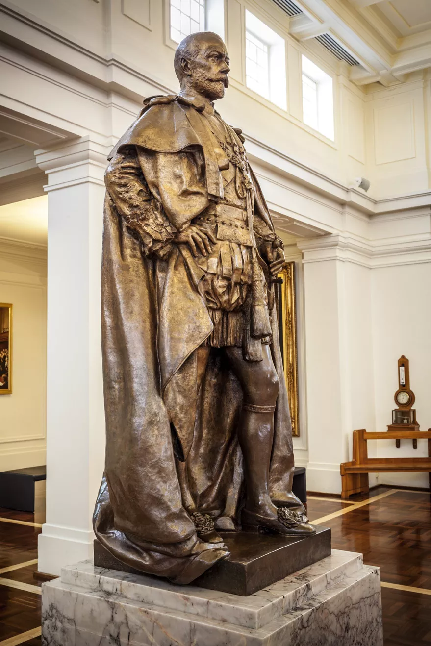 A bronze statue of a man with a cloak on a marble pillar in a room with timber floors. A bronze statue of a man with a cloak on a marble pillar in a room with timber floors.