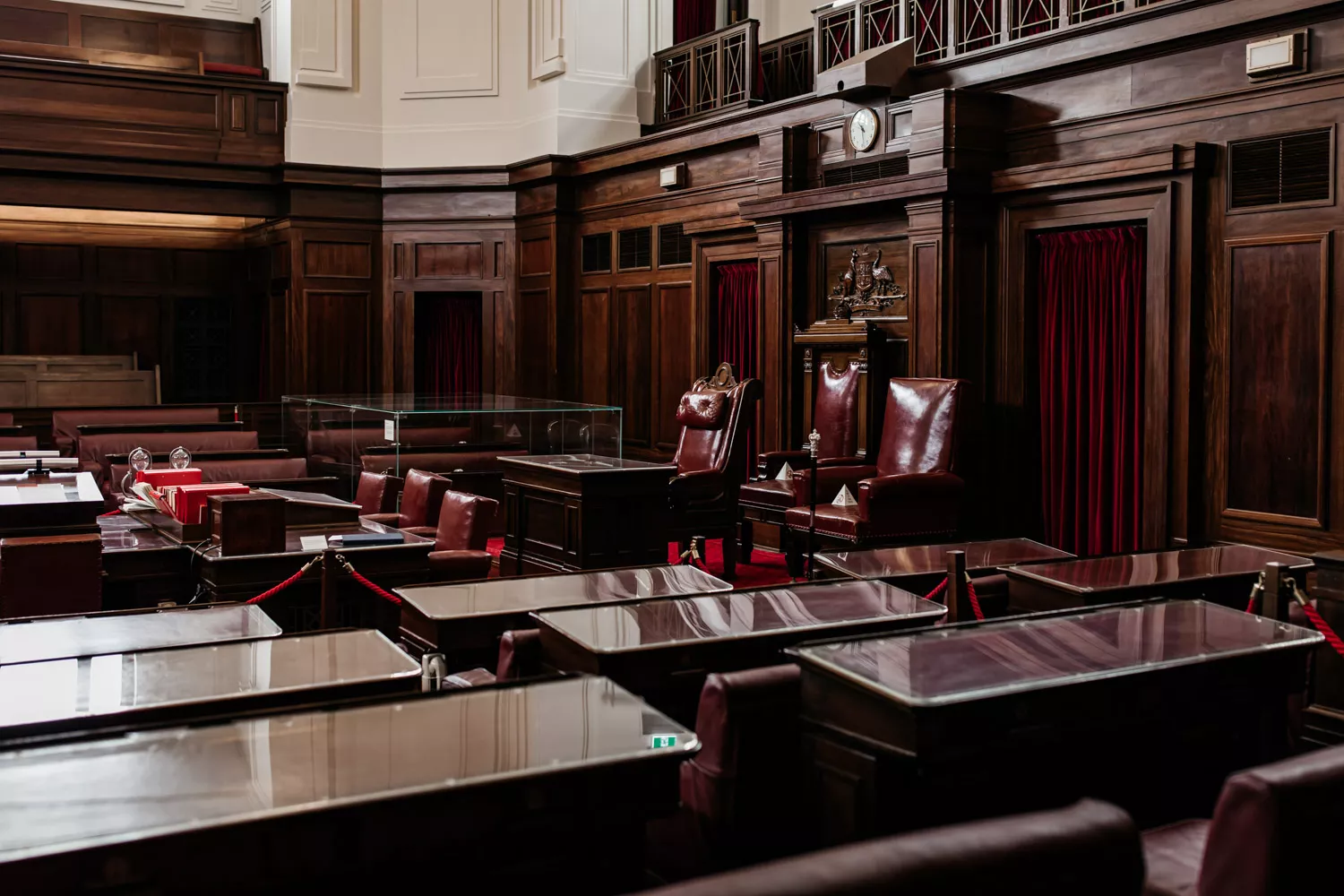 A room with rows of glass topped benches facing a red leather chair, with red curtins and timber panelling.